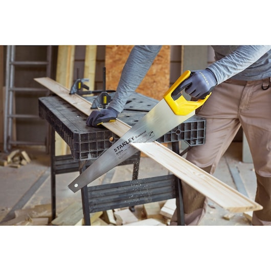 STANLEY STHT20350-1 hand saw with yellow handle cutting wood plank in workshop, photography category.