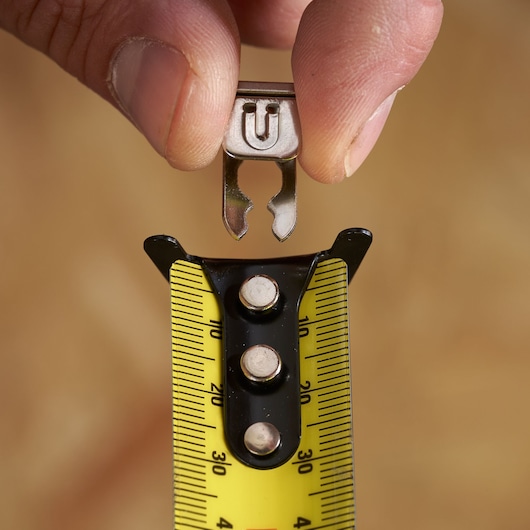 Close-up photo of STANLEY STHT37240 tape measure hook being attached to yellow tape in photography setting.