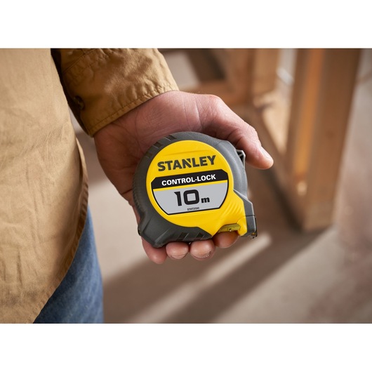 Photo of STANLEY STHT37241 tape measure, yellow and gray, 10m length, held in hand.