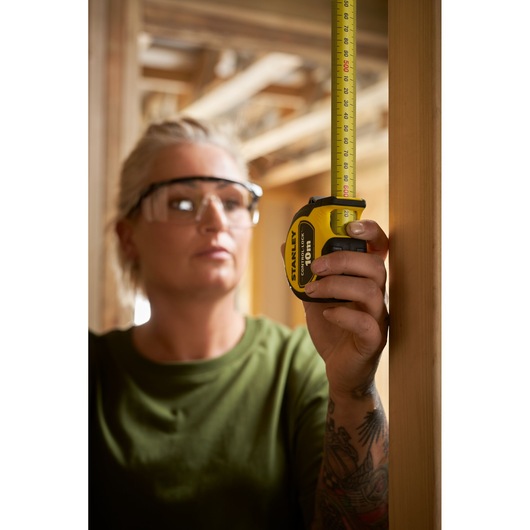 Photo of a person using a STANLEY STHT37241 tape measure to measure a wooden beam in a construction setting.