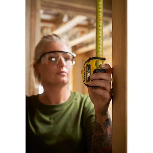 Photo of a person using a STANLEY STHT37241 tape measure to measure a wooden beam in a construction setting.