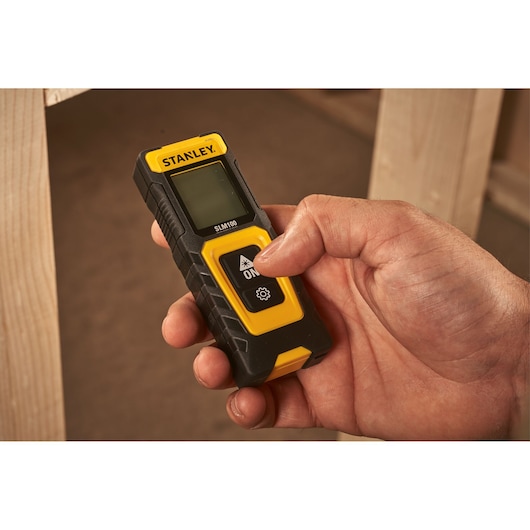 Photo of STANLEY STHT77100-0 digital laser distance measurer held in hand, black and yellow design.