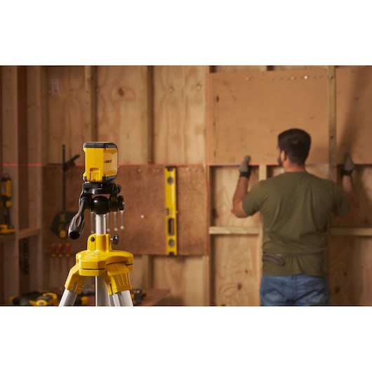 STANLEY STHT77611-0 laser level on tripod projecting line, builder working in wood room background.
