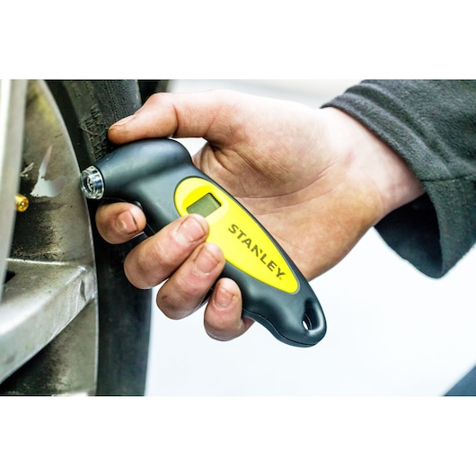 STANLEY STHT80874-0 tire pressure gauge held by hand next to car wheel.