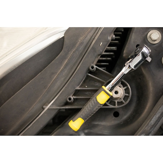 STANLEY STMT82663-0 ratchet with yellow and black handle used on engine part, close-up photography.