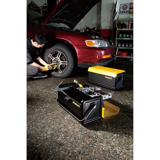 Photo of STANLEY STST1-75509 toolbox open with tools, yellow and black, beside a mechanic working on a car.