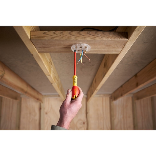 Photo of a hand using STANLEY XTHT0-62692 insulated screwdriver on ceiling wiring, indoor construction setting.